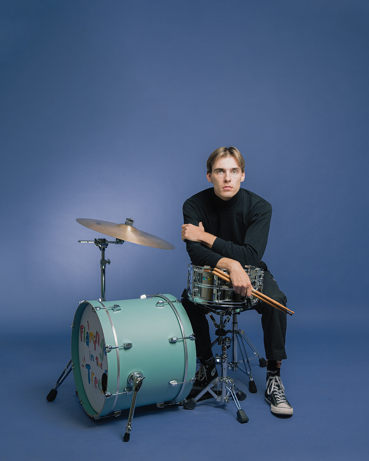 Musician seated at a drum kit in a blue studio