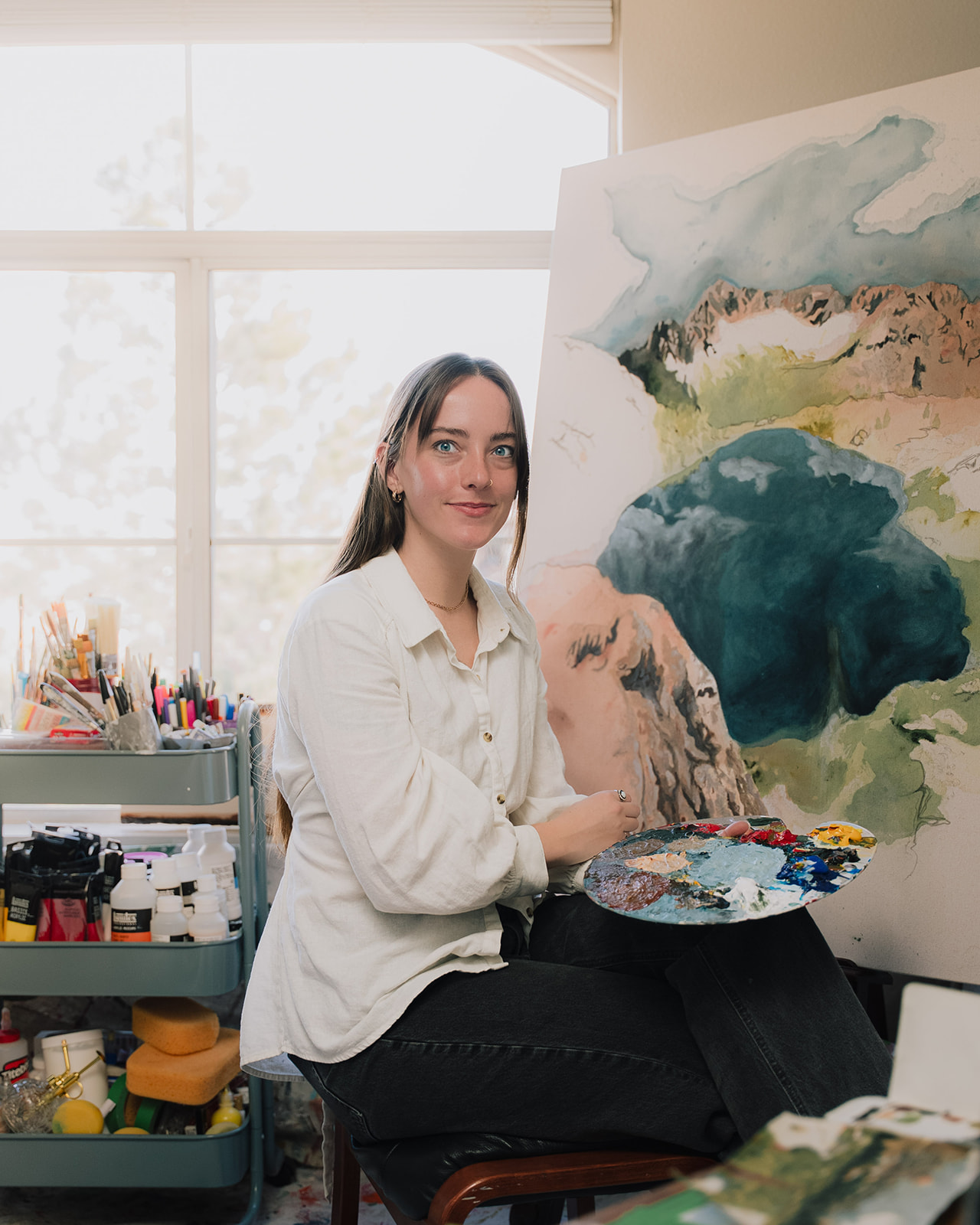 Artist portrait of Haley holding a paint palette beside her canvas